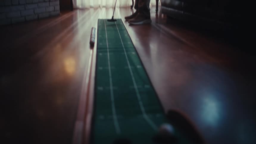 Man holds a golf club as he putts a ball in his living room