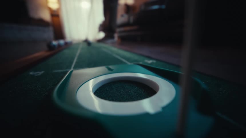 Man playing indoor golf putts the ball into the hole