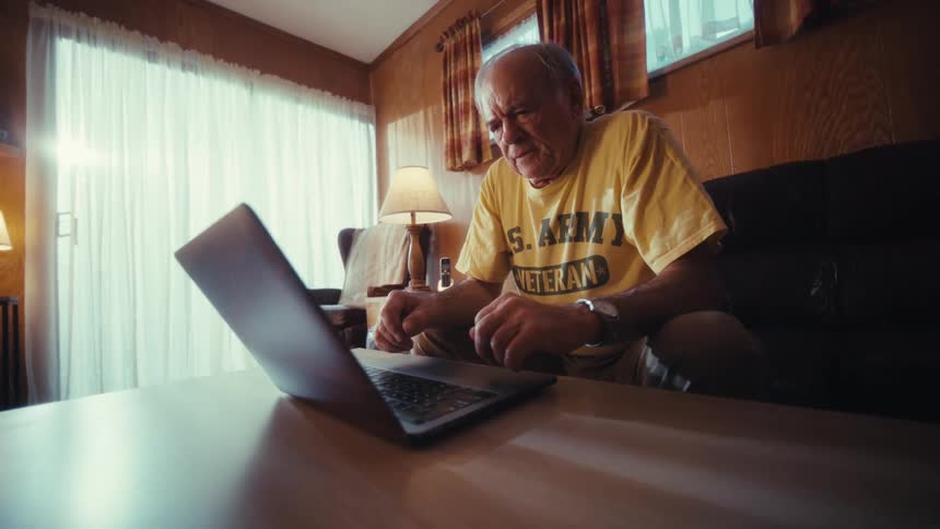 Elderly man sits down opens his laptop and begins to type
