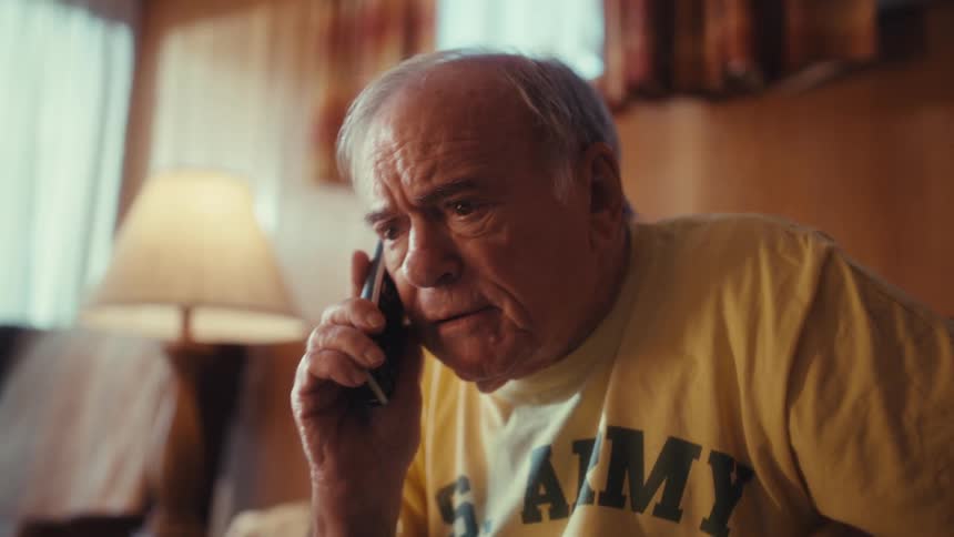 Elderly man on the phone conversing euphorically while seated in front of a laptop