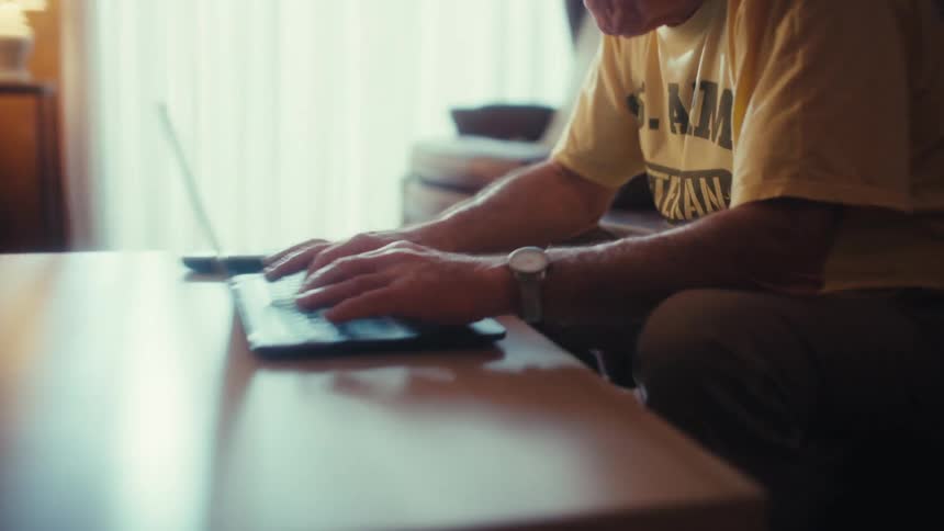 Man sitting on his living room couch typing on a laptop computer
