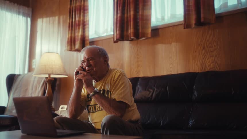 Elderly man is sitting in his living room talking on a phone