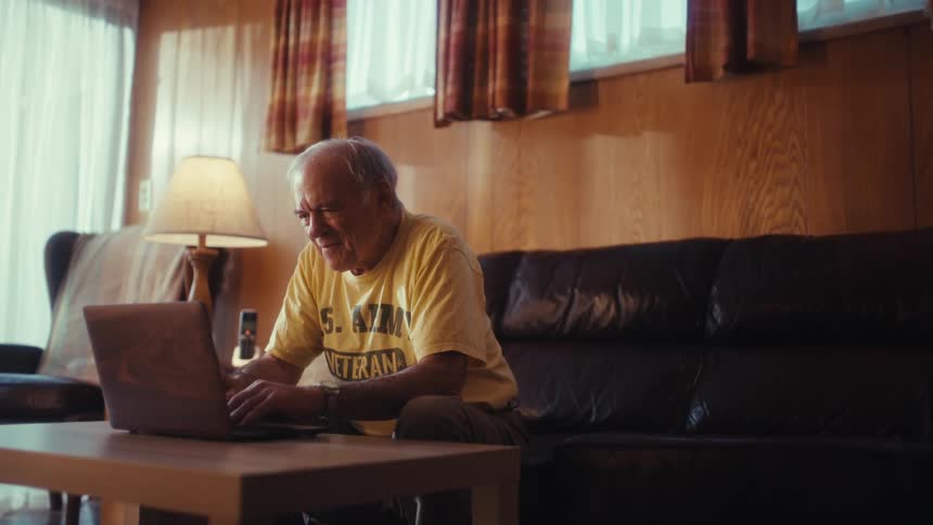 The man leans forward on his couch while typing on his laptop