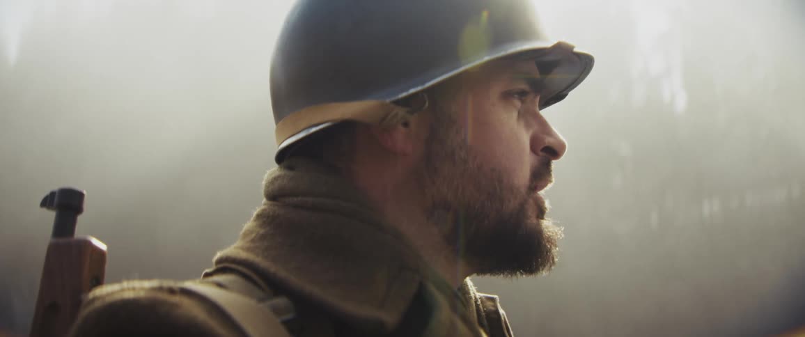 A bearded soldier wearing a helmet and winter gear stands in a misty forest looking toward the sky with a stunned expression as his breath frosts in the cold air