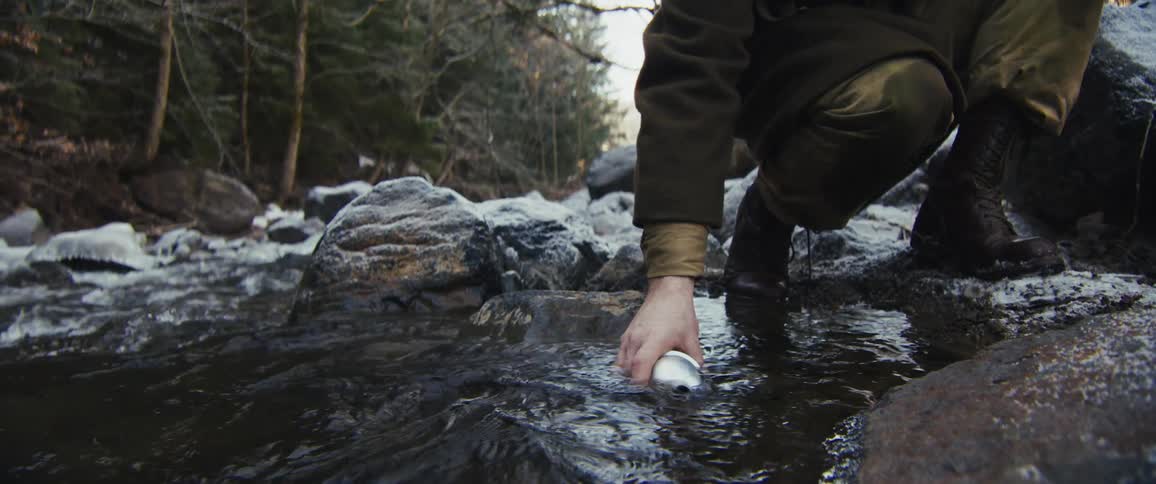 A person filling a water bottle from a stream