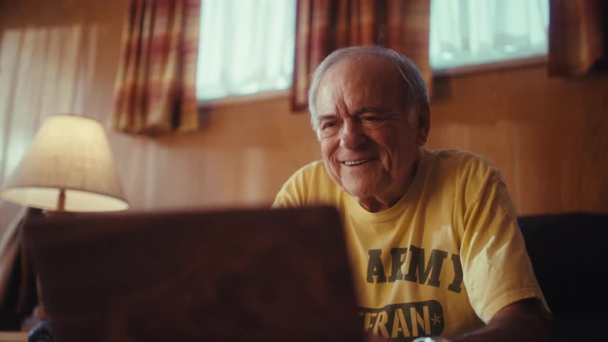 The man is smiling as he types on his laptop