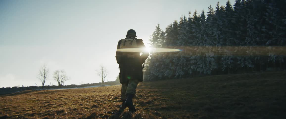 Soldier walking in a natural area with a coniferous forest in the background