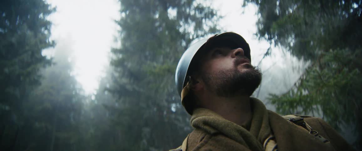 A military soldier in uniform and helmet standing in a forest at midday scanning the surroundings