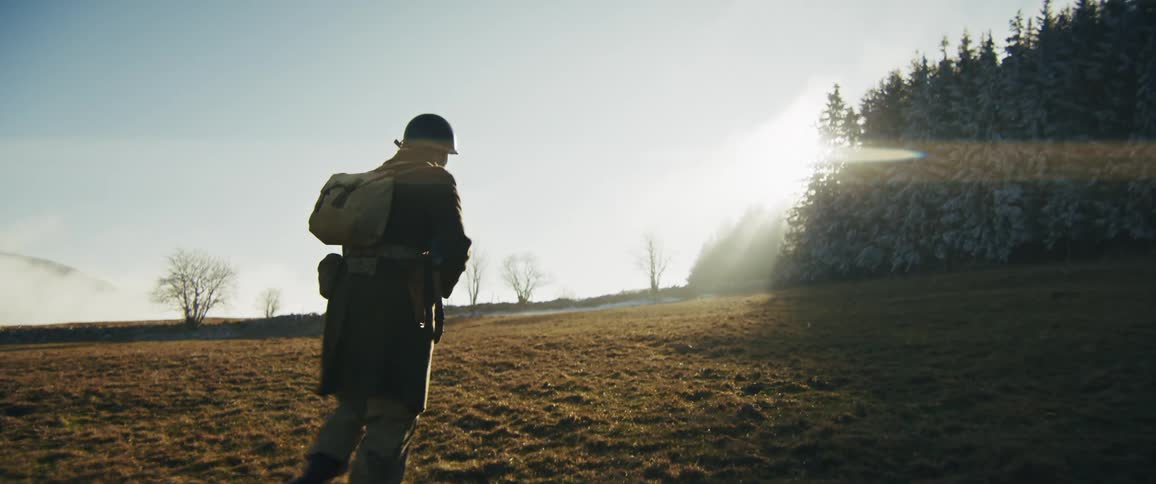 The soldier is walking towards the forest on the field