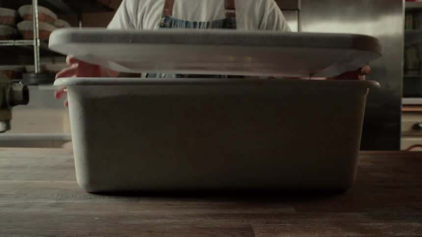 The man removes the lid from the container in the kitchen