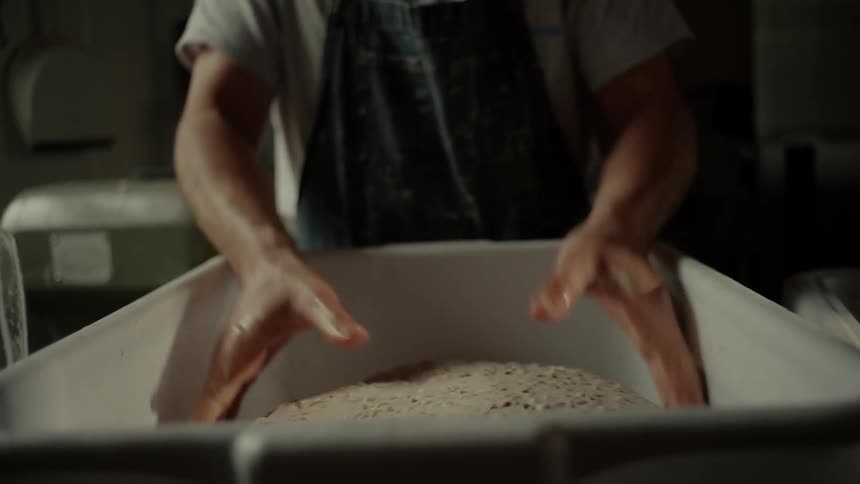 Bread dough being shaped by hand inside a container in a preparation environment