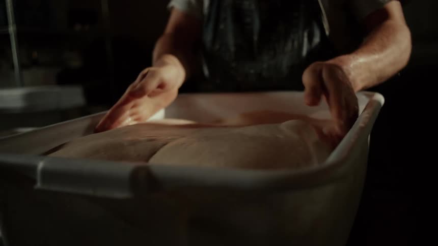 The man is flipping large amounts of dough in the container