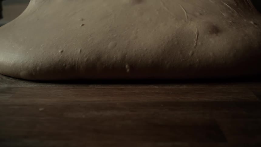 Dough placed on a wooden table slowly sliding across the surface