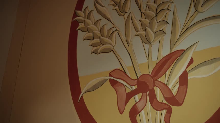 Mural painting with stylized flowers tied by a ribbon in warm tones over a geometric background