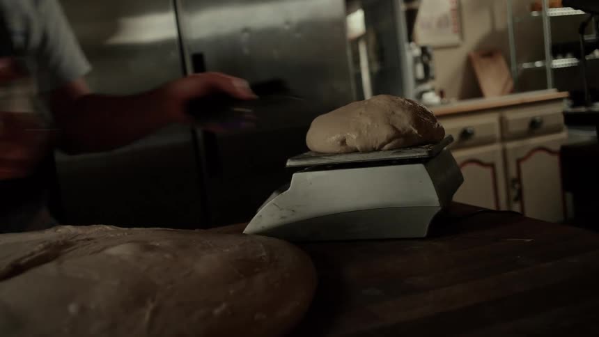 A male chef making dough inside a bakery taking a chunk and weighing it on a scale