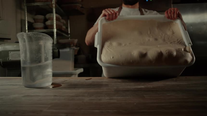 A man dumping a tray of dough onto a counter