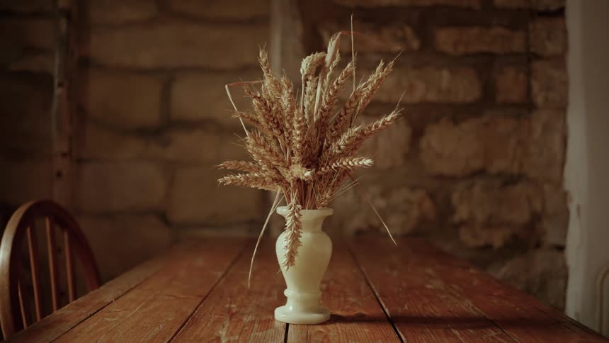 A small flower vase with a plant in it placed on a wooden dining table with a chair beside it