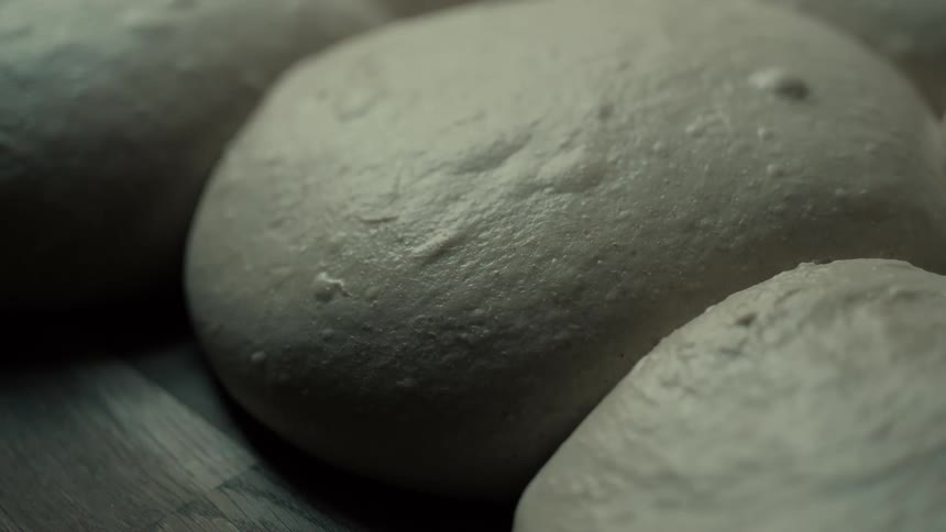 Fresh raw dough balls resting on a dark wooden surface ready for baking in a professional kitchen environment