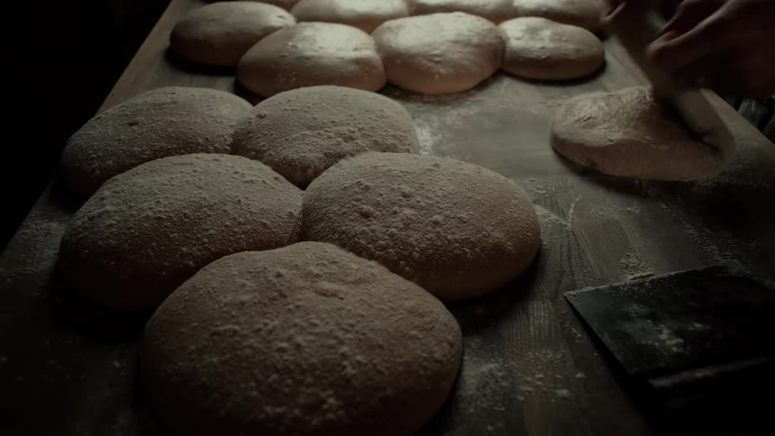 A chef picking a piece of dough from a row of dough portions and molding it by hand on the countertop