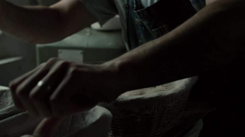 In a dimly lit bakery a bakers hands carefully lower a shaped round of dough into a clothlined proofing basket settling it gently next to others