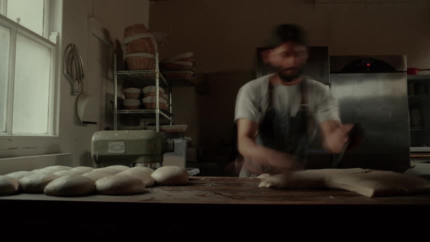 Man at a workbench cutting bread dough