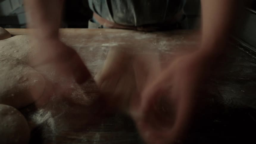 Shown in a fastpaced stuttering motion a bakers hands vigorously knead and shape a mound of dough on a flourdusted wooden workbench