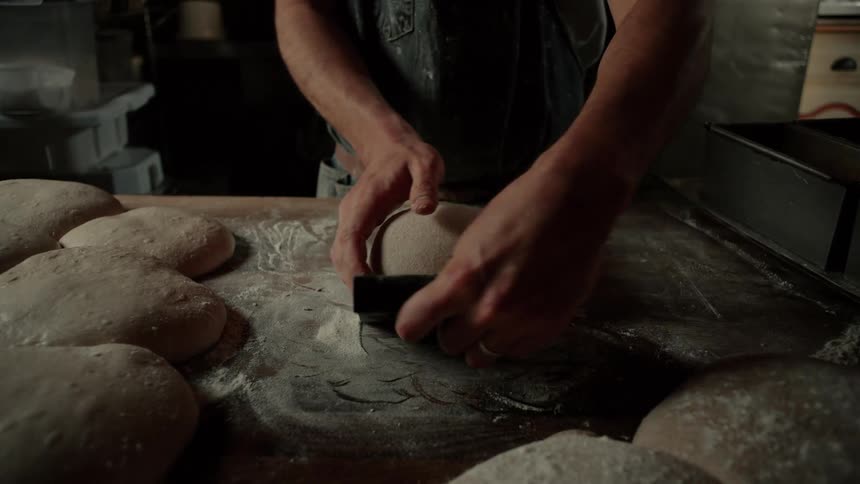 A chef molding dough and placing it on a pan inside the kitchen ready for the oven