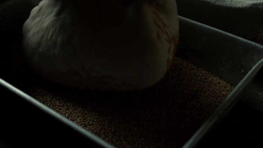 Bread dough being coated with seeds inside a preparation container