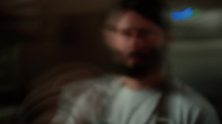 A blurred view of a male worker in an apron moving around a kitchen area with shelves and workstations in the background