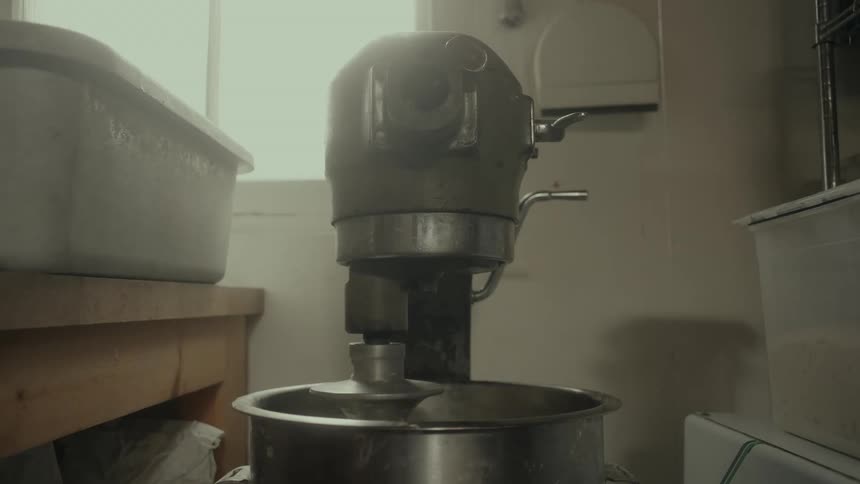 An electric mixer spinning as it mixes dough inside a bakery