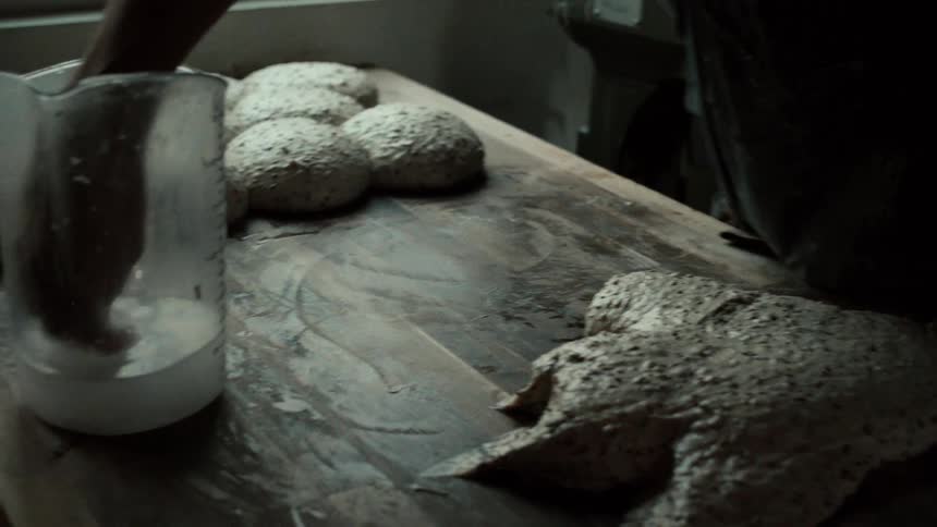 Hands using a spatula to prepare bread dough on a wooden work surface