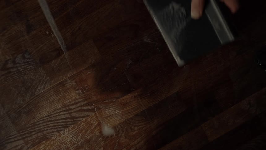 Hand with spatula removing white liquid from a wooden countertop
