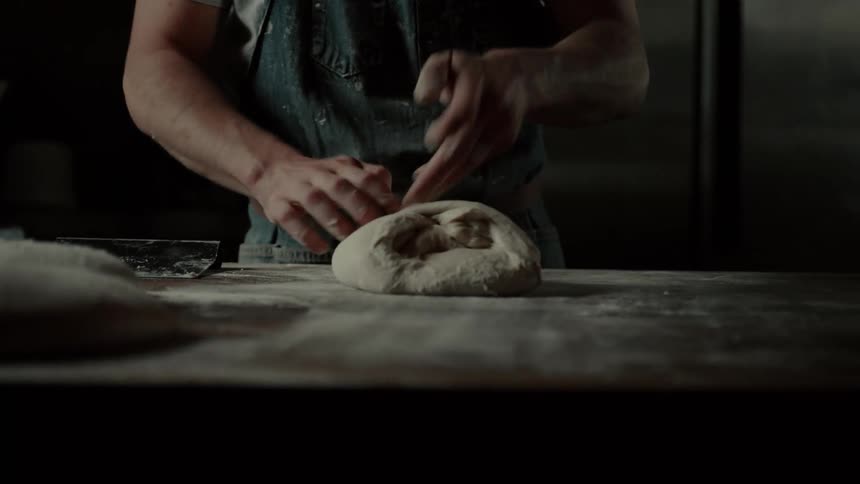 Person preparing bread dough at a table with wheat flour