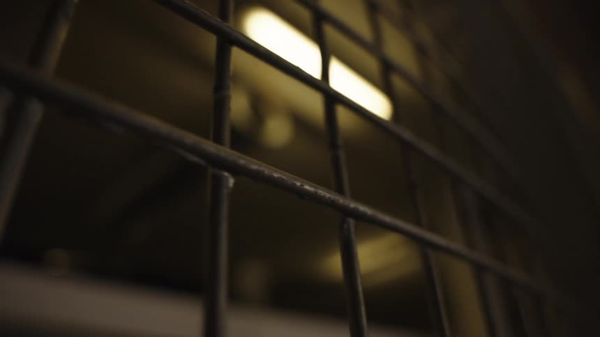 A close view of a dark metal security grate with a bright fluorescent light glowing in the background
