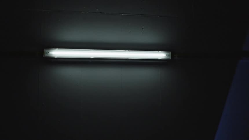 Single bright fluorescent light fixture glowing against a dark textured ceiling captured from a low angle