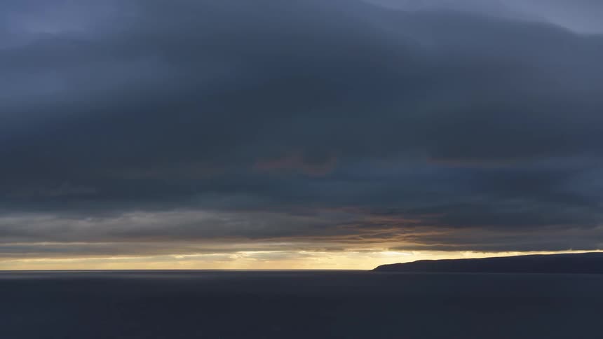 Dark clouds hang low as they move over the coast at sunrise