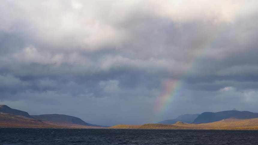Rainbow stretches over the land along the coast with mountains in the distance