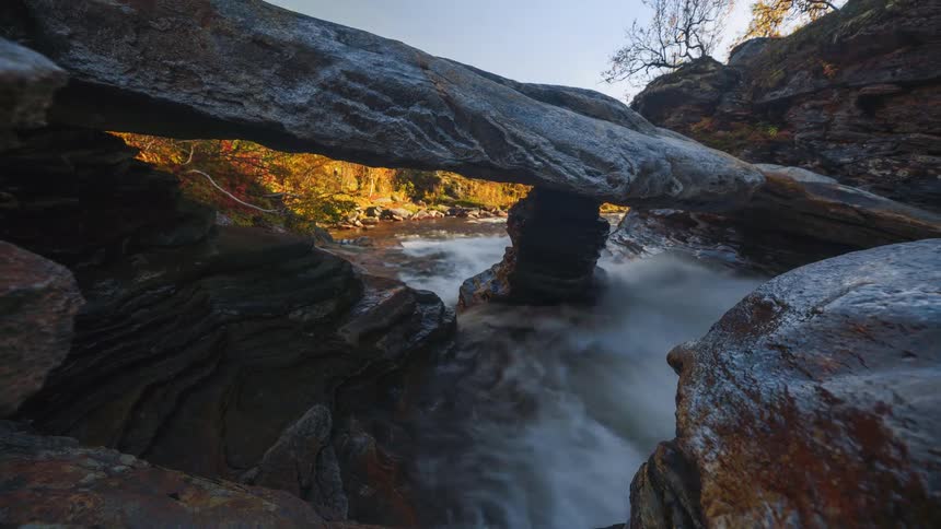 A rocky terrain with a fastflowing stream cutting through it at midday sunlight highlighting the moving water and uneven stones