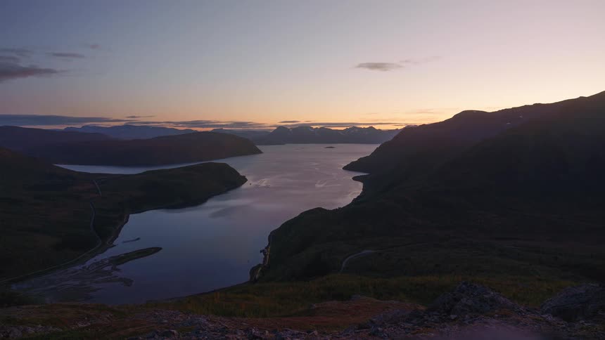 A lake surrounded by a mountain range in the wilderness the setting sun disappearing behind the peaks as the atmosphere grows dark