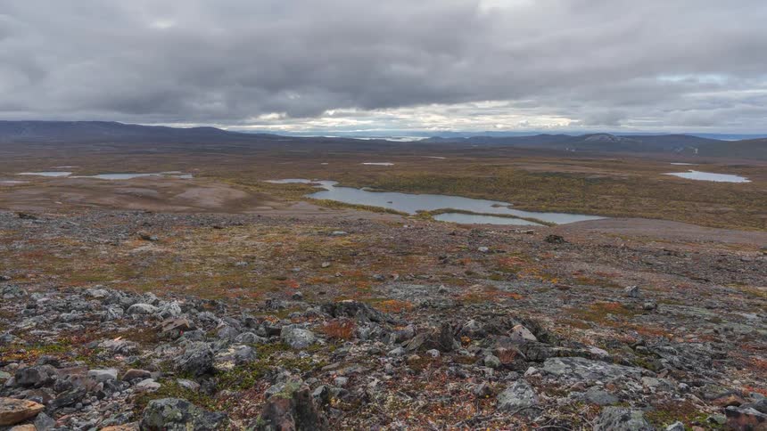 Rocks on a hill overlooking ponds with mountains in the distance under a cloudy sky