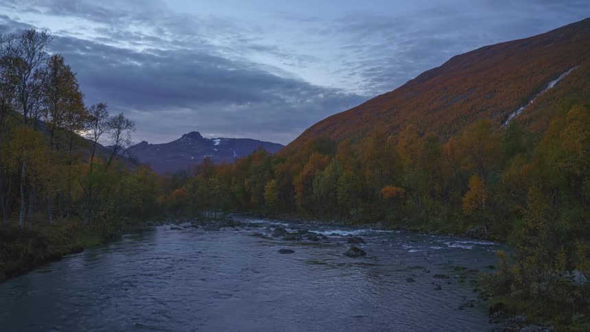 A stream flowing through the wild with a grasscovered mountain rising beside it on a cloudy day