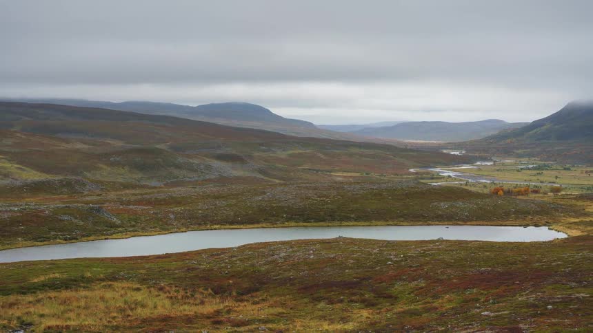 Day turning to evening in the wilderness with a surrounding mountain range and a lake in the midst under a cloudy sky