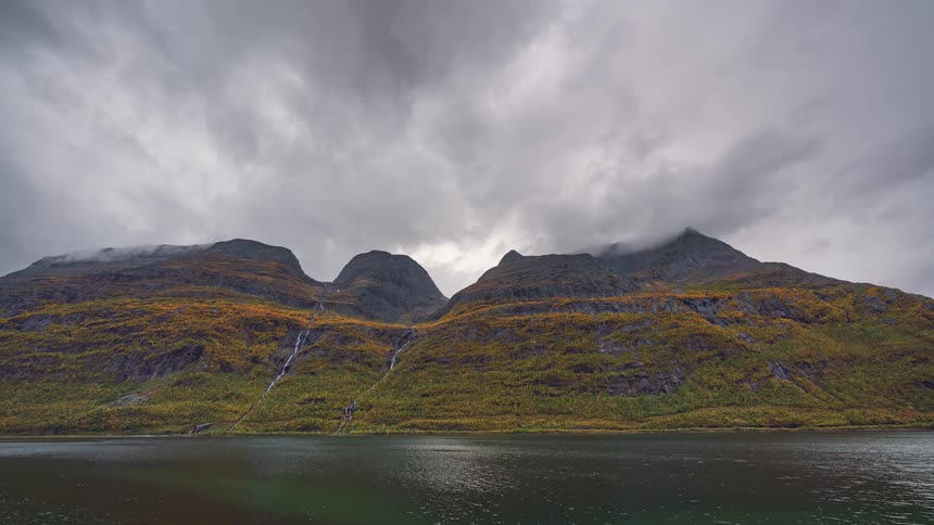 The water passes by the cloud covered mountain