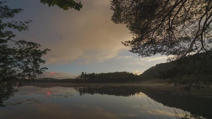 Forested mountains along the coast as the sun shines and clouds reflect on the water as they move across the sky