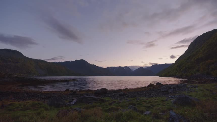 A lake surrounded by mountains as the day shifts from sunset to darkness the sun disappearing behind the peaks and the environment gradually dimming