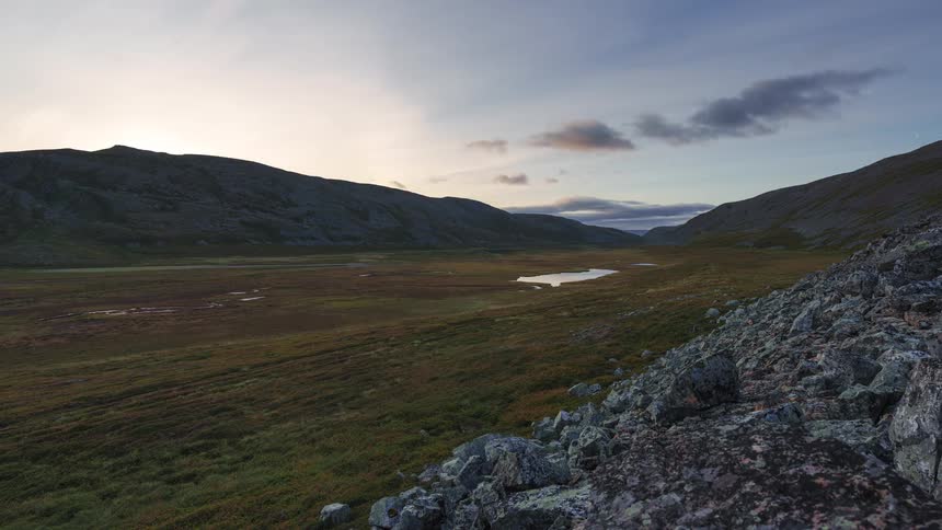 Open land with a pond between mountains as clouds move across the sky as darkness falls