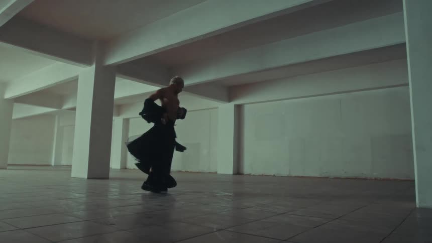 Male dancer wearing black flowing clothes dances in a large empty white room