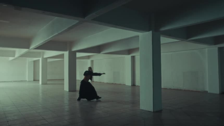 Person dances alone in a large indoor space with structural columns and a concrete floor