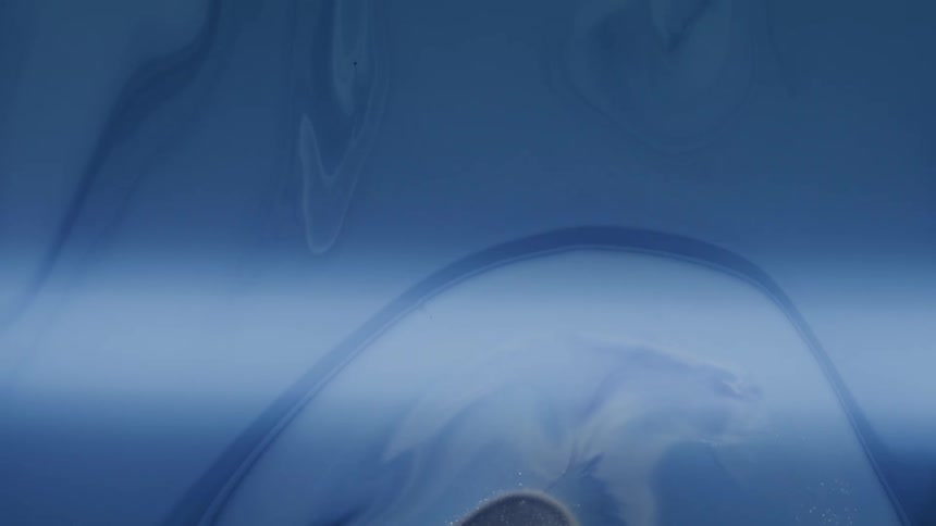An abstract ethereal composition features layered flowing blue and indigo forms resembling liquid or ink suspended in water with fine sparkling particles scattered across the lower half