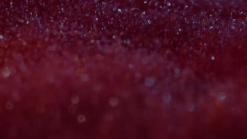Particles mostly reddish and some sparkling fly into the air as the mass is shaken